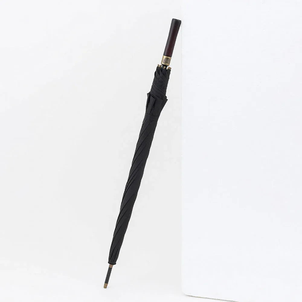 The closed black premium big rain umbrella standing against a white corner, highlighting its length.