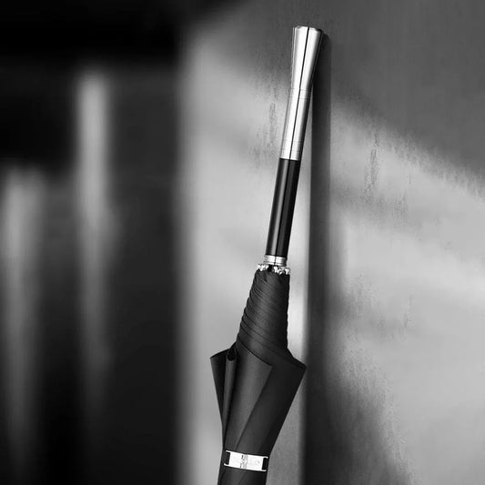 Monochrome lifestyle shot of the closed premium long handle umbrella with an alloy handle leaning against a wall.