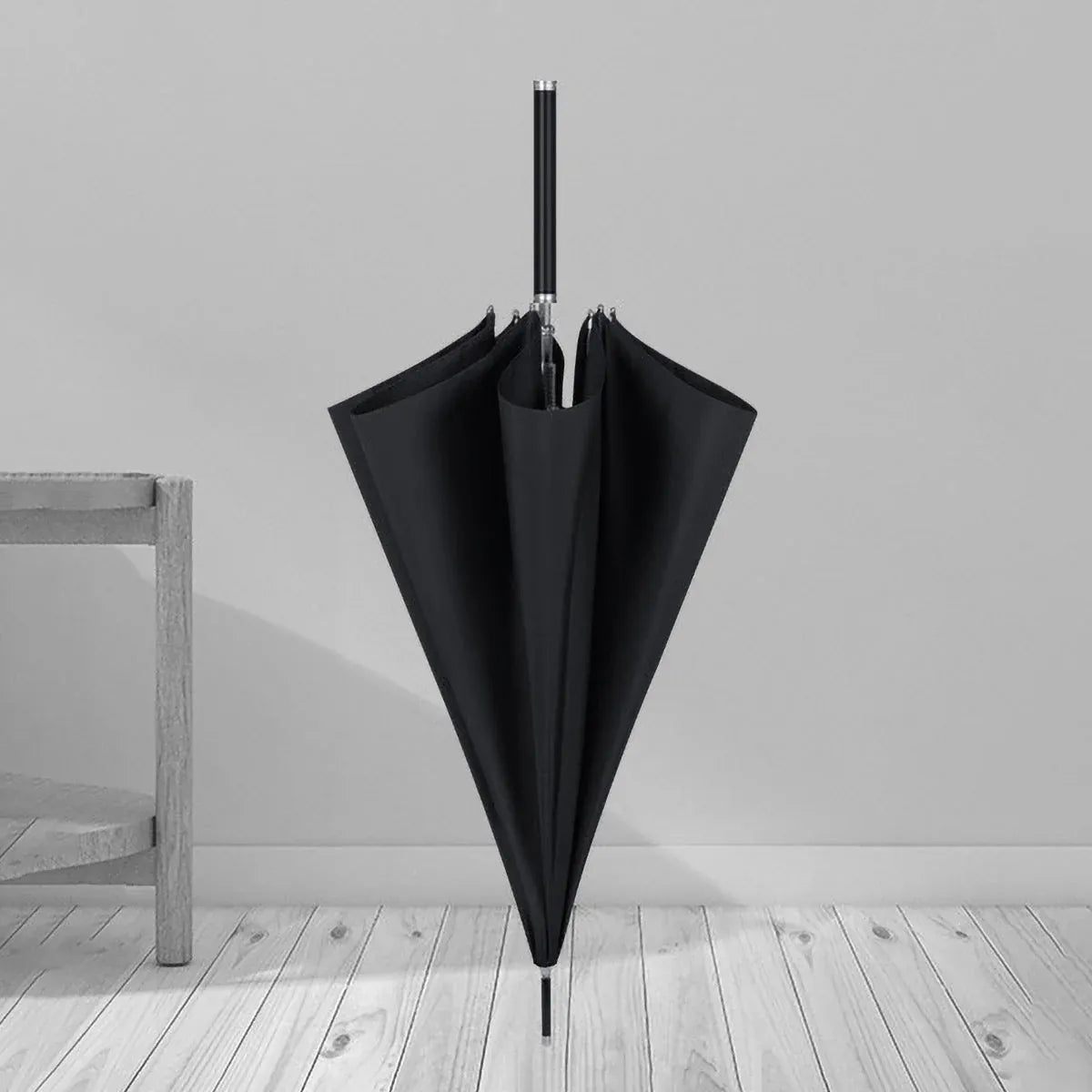 The closed black premium long handle umbrella standing on a wooden floor in a room setting.
