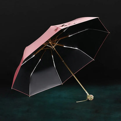 The open pink Prestige folding umbrella with its crystal-embellished gold handle, showcasing the black interior lining.