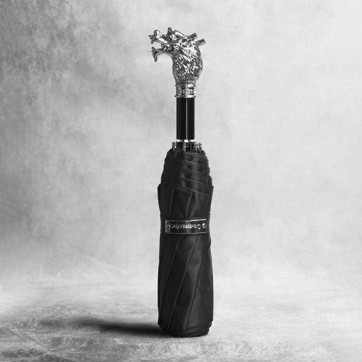 The closed silver animal head folding umbrella with the Dragon handle against a textured background.