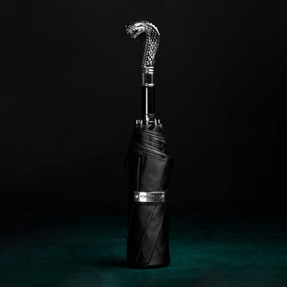 The Silver Cobra Head folding umbrella standing closed against a dark background, showing the handle detail.