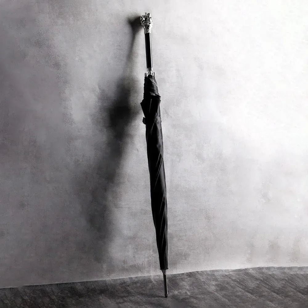 The Silver Lion Head umbrella standing closed against a textured wall, showcasing its length and handle.