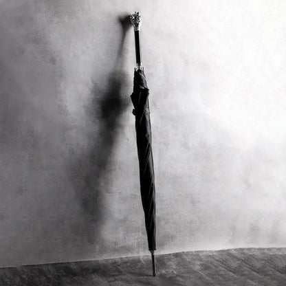 The Silver Lion Head umbrella standing closed against a textured wall, showcasing its length and handle.